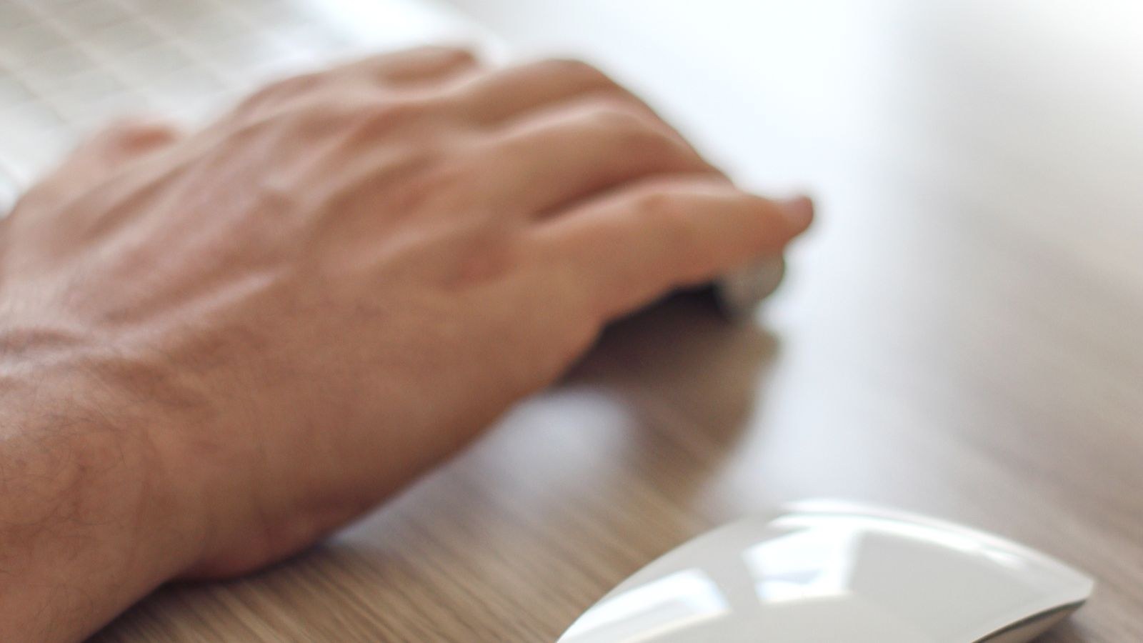 Close-up of a hand at a minimalist desk using a sleek white mouse