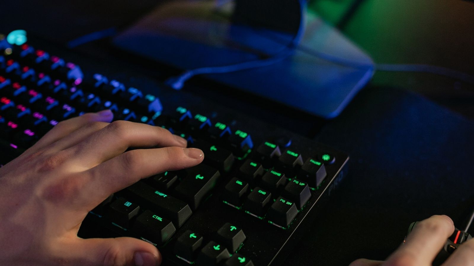 Hands using a keyboard and mouse on a large desk pad with coloured lighting