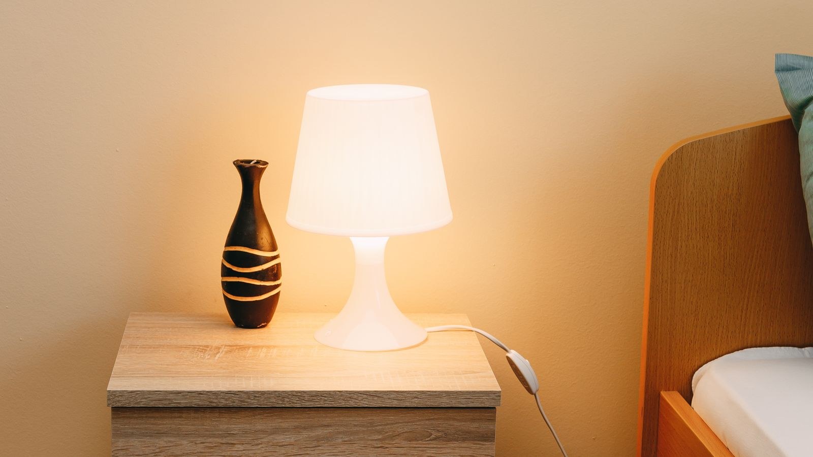 Wooden nightstand with a lamp and vase positioned at mattress height