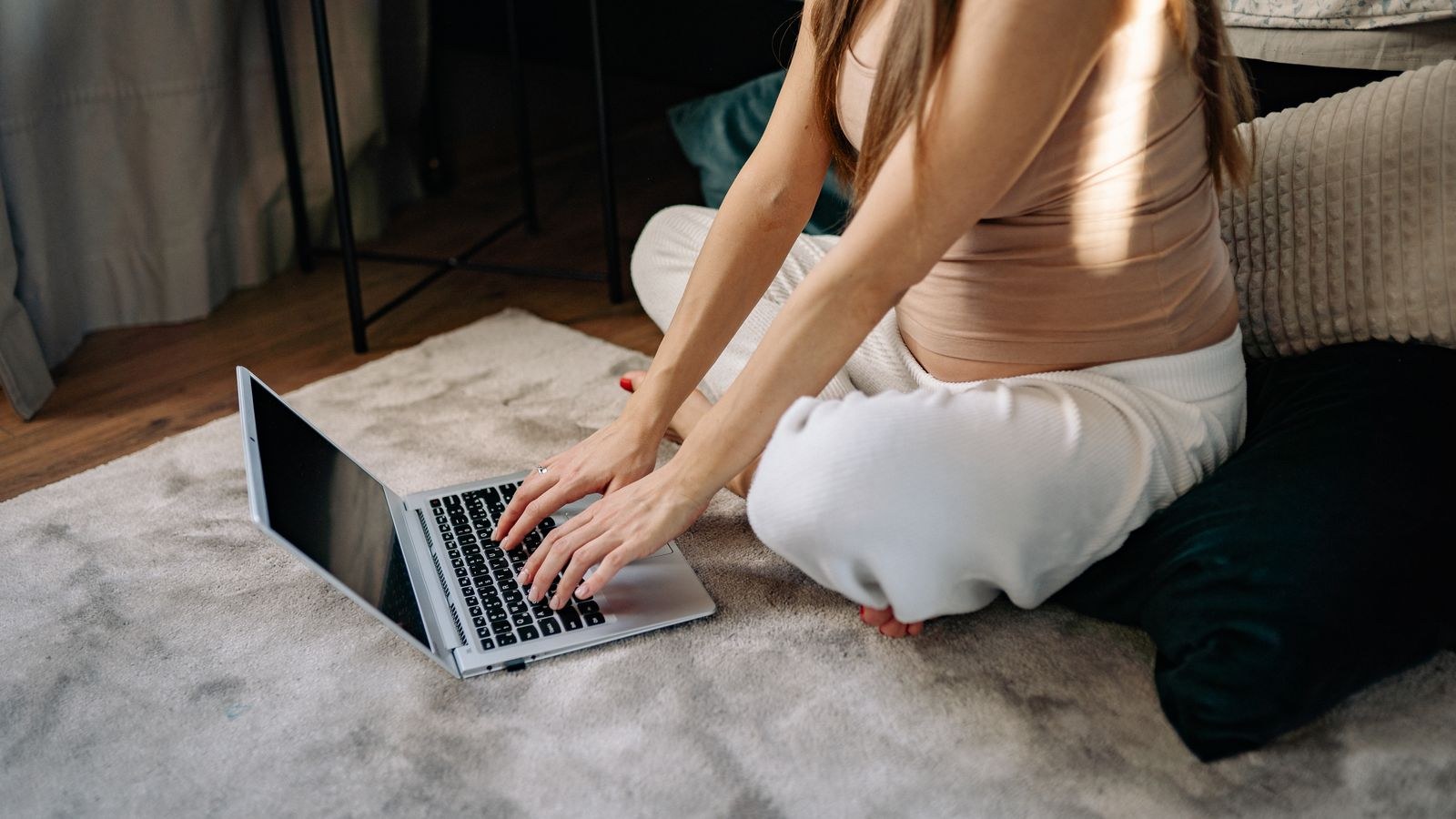 Pregnant woman working at a laptop in a sunlit home workspace with a supportive seat