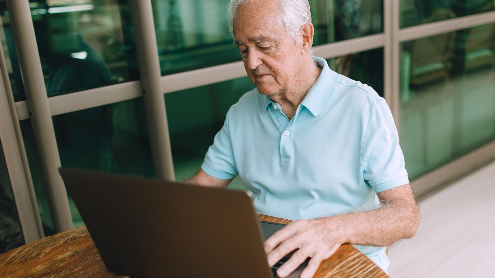 Senior man seated at a wooden desk using a laptop in a comfortable chair