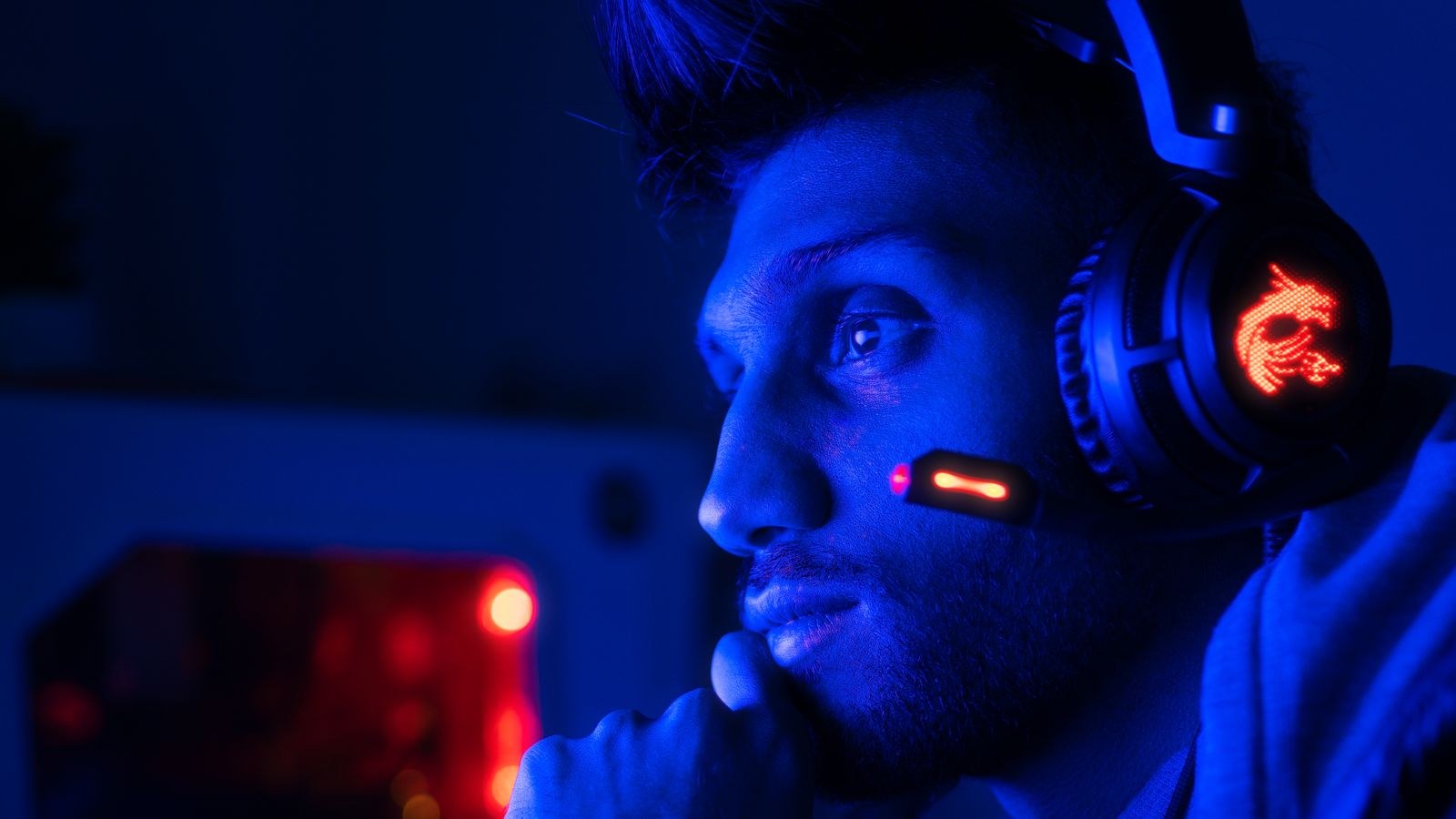 Focused gamer wearing a closed back gaming headset in blue lighting