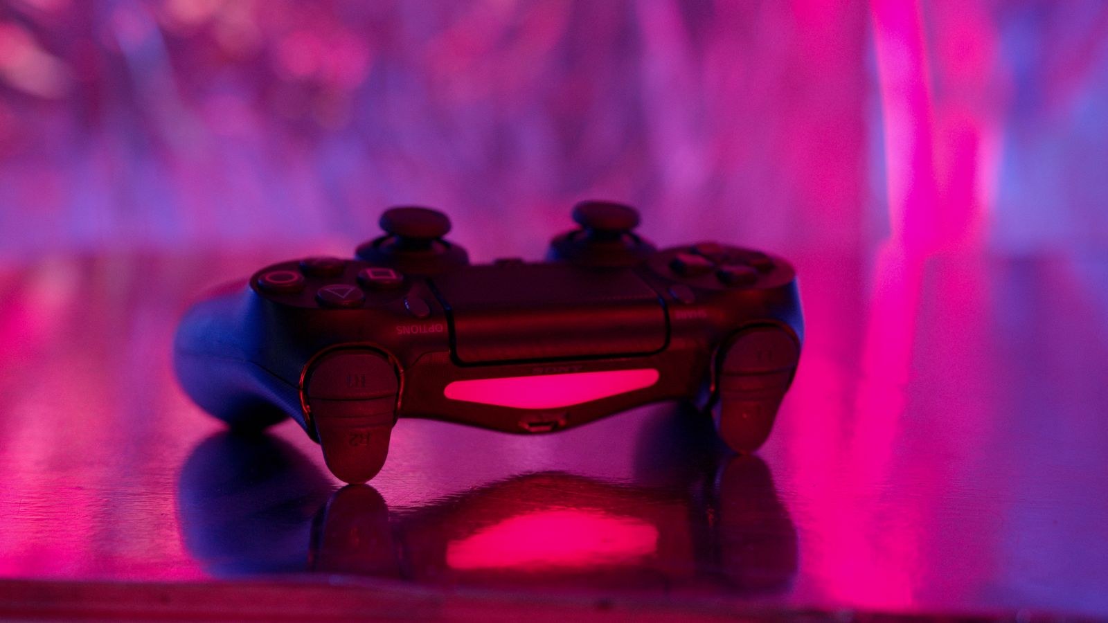 Wireless game controller in focus against a pink and purple neon background