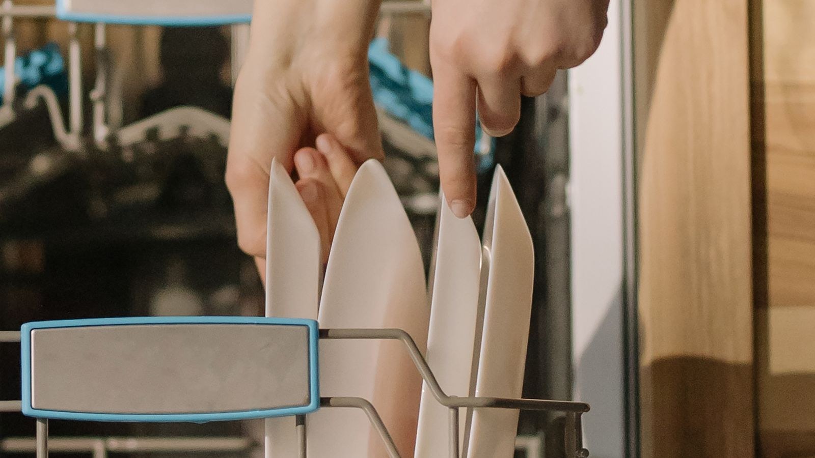 Hands loading clean dishes into a small open dishwasher