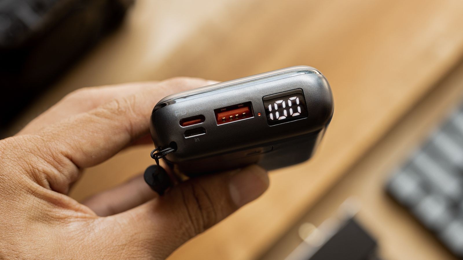 Hand holding a power bank showing a full charge on its digital display