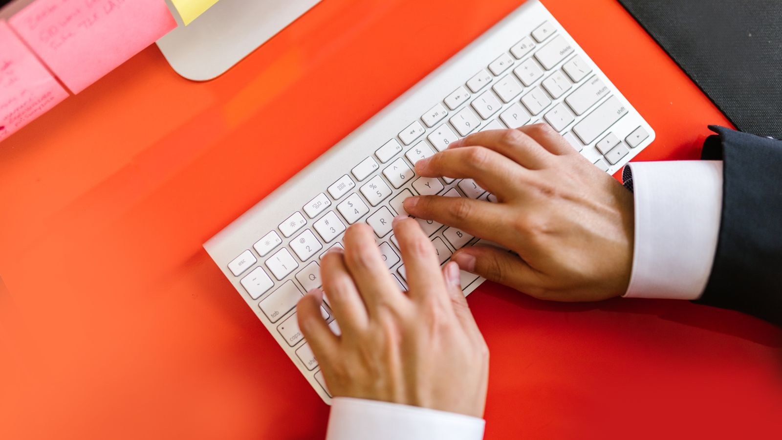 Close up of hands on a wireless keyboard positioned close to the edge of an orange desk