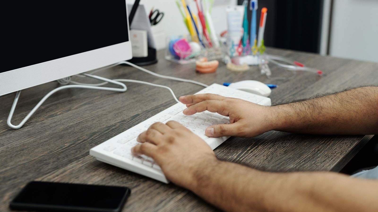 Hands typing on a white keyboard at a wooden desk demonstrating a flat wrist angle