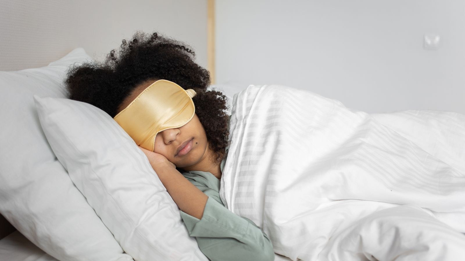 Woman sleeping peacefully with an eye mask in a bright white bedroom