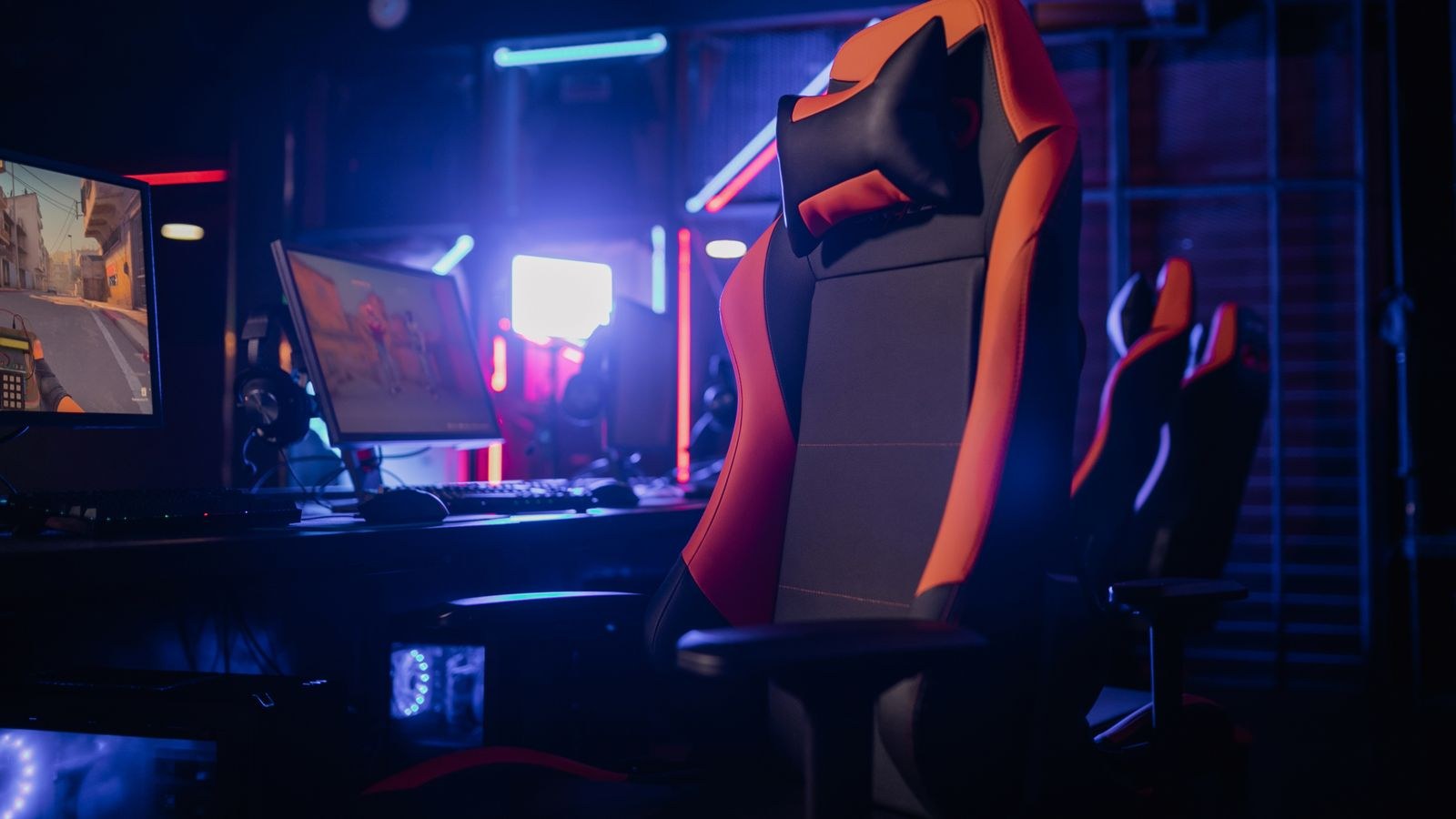 Gaming setup with a sleek chair and computers under coloured lighting