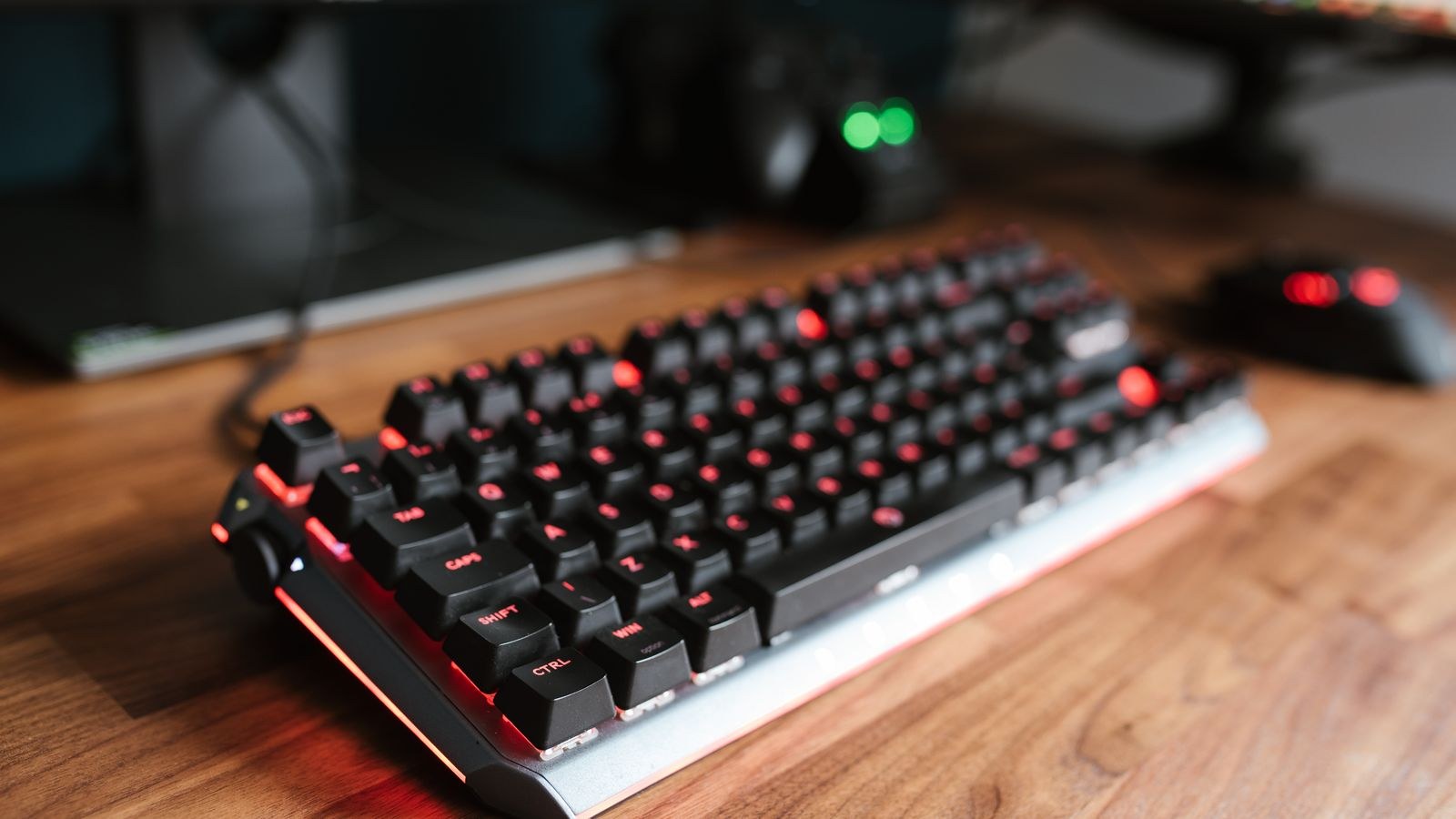 Backlit keyboard on a wooden desk next to a mouse and laptop