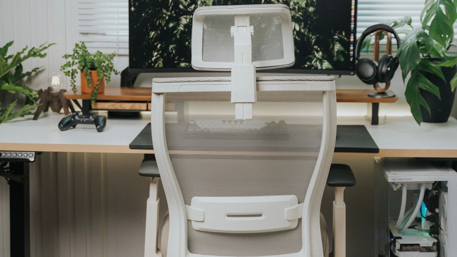 White ergonomic office chair with contoured armrests beside a large monitor and plants