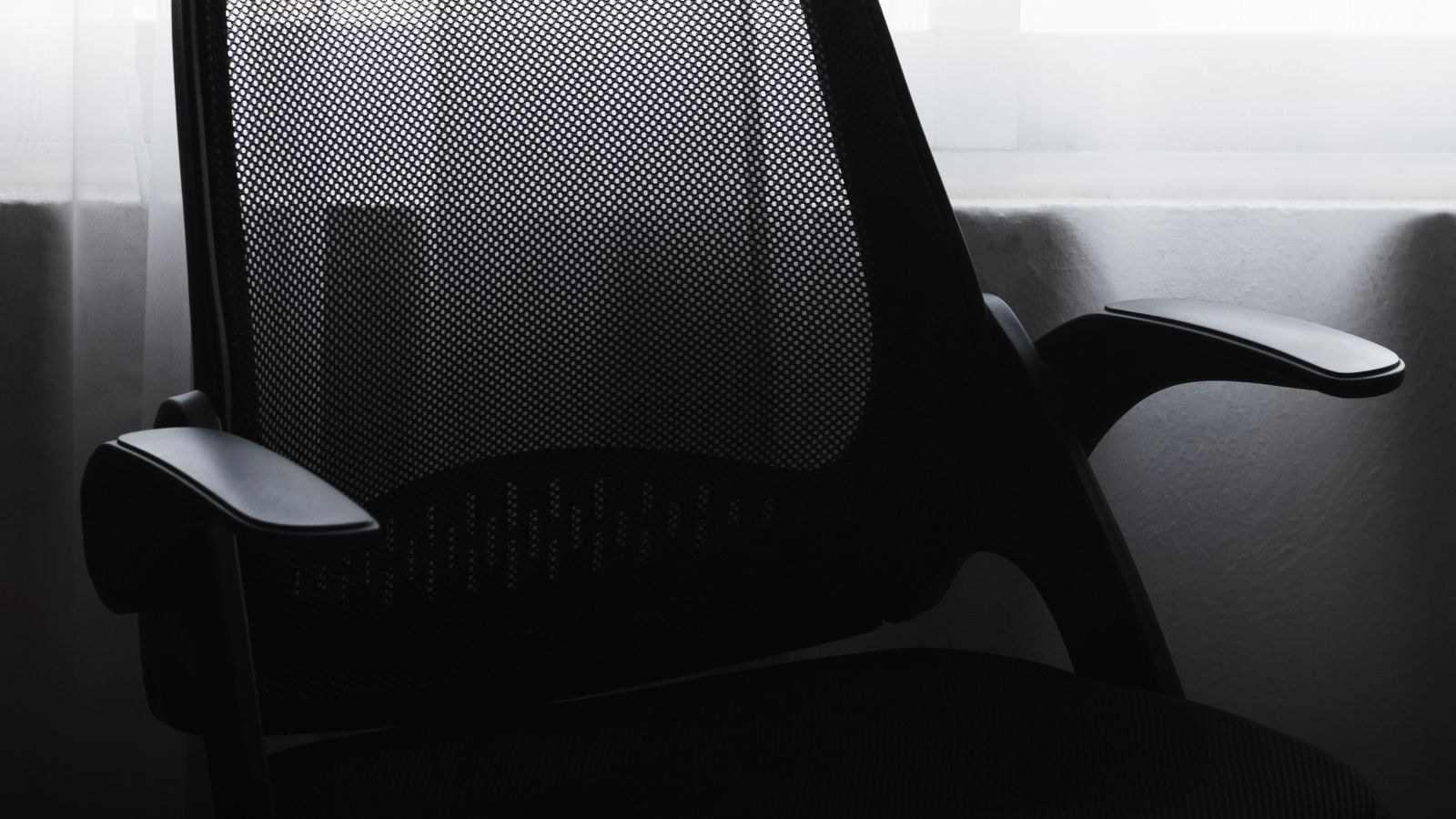 Black mesh office chair silhouetted in a minimalist workspace showing its rolling base