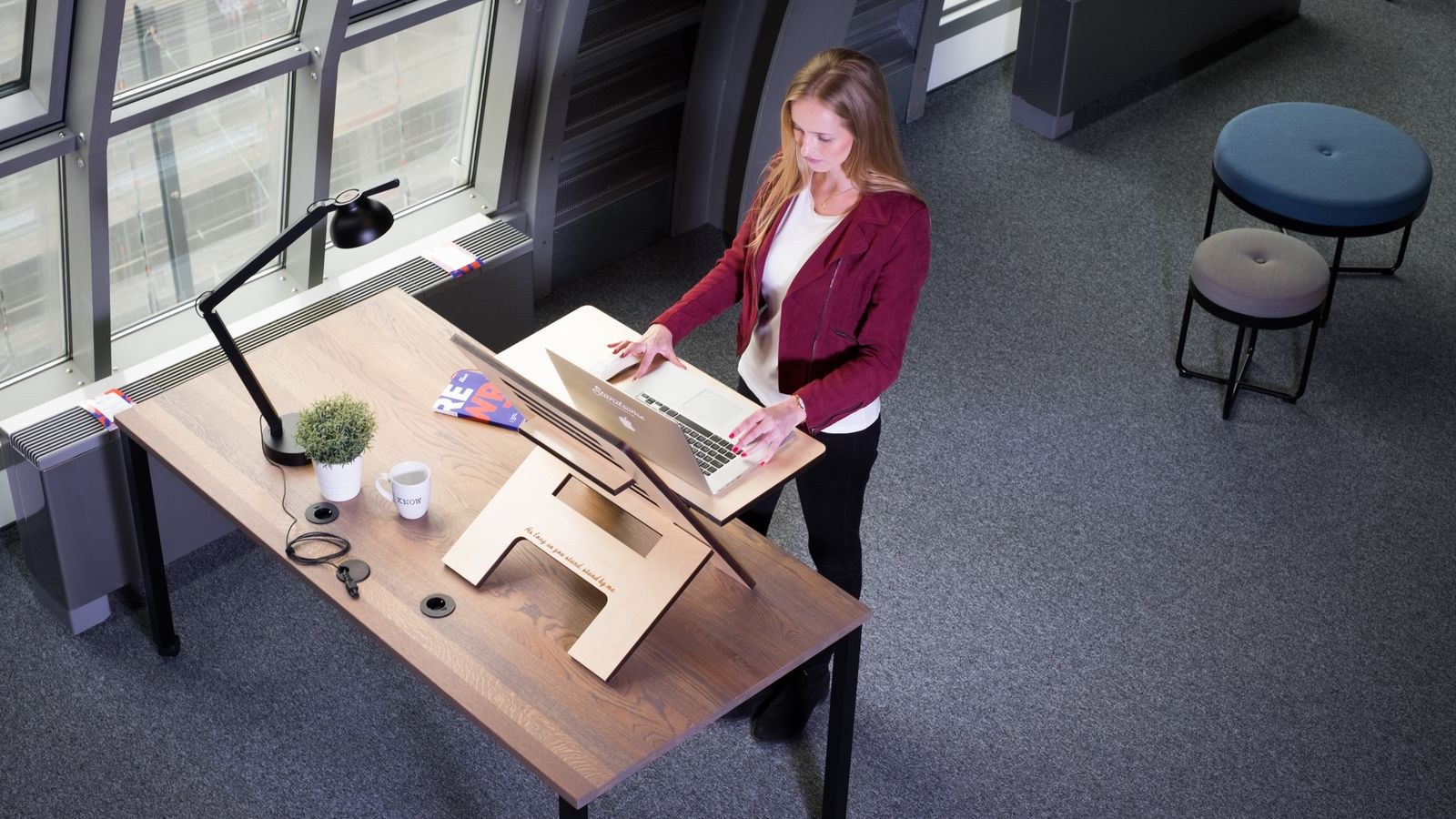Woman working at an adjustable standing desk with a laptop in a modern office