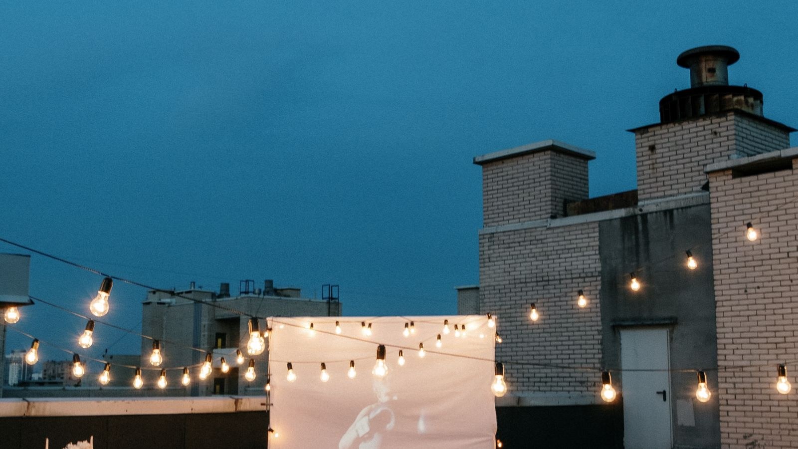 Friends watching an outdoor movie under string lights on a warm evening