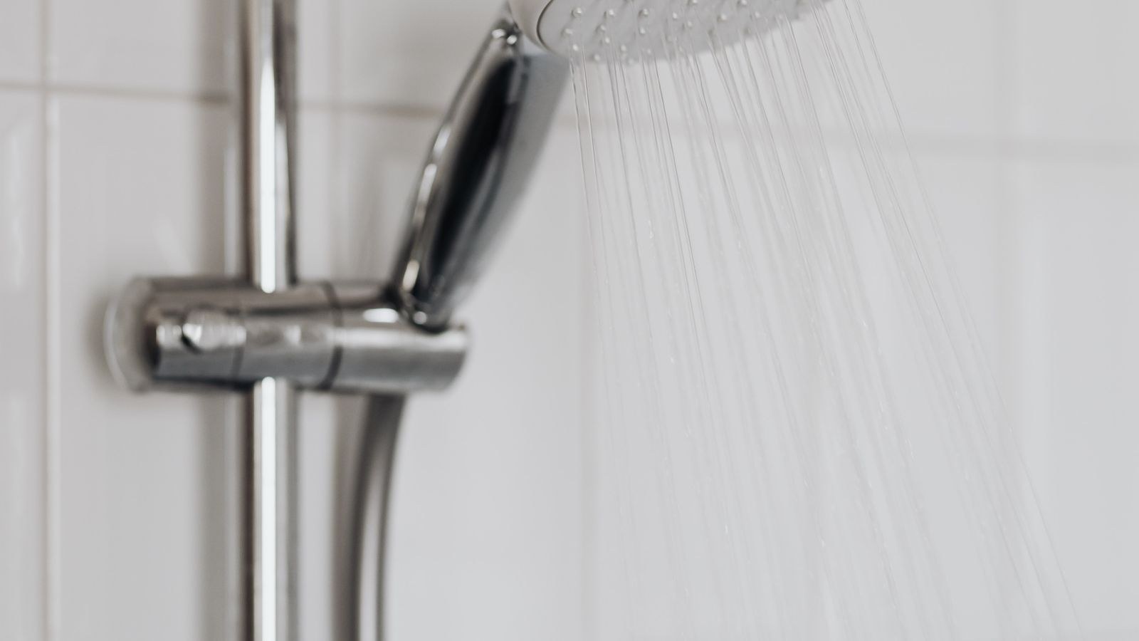 Close up of a chrome shower head with water flowing in a modern bathroom