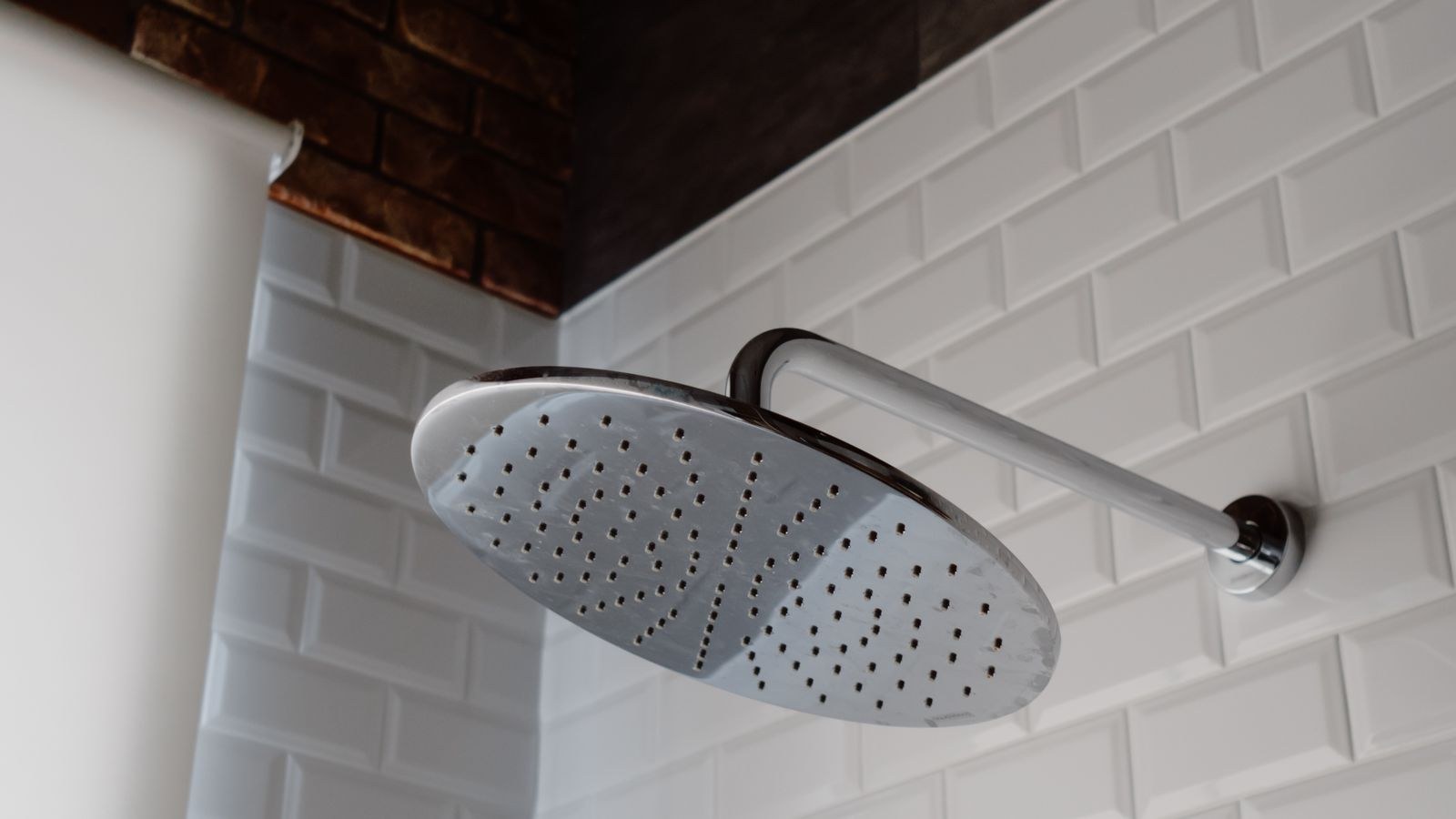 Sleek stainless steel shower head installed against white bathroom tiles