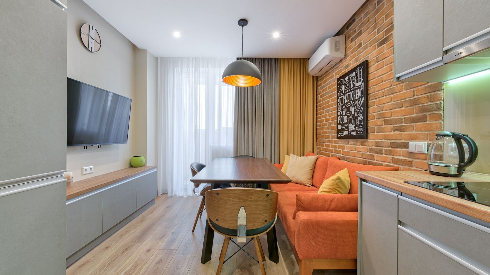 Small apartment living area with orange sofa against an exposed brick wall