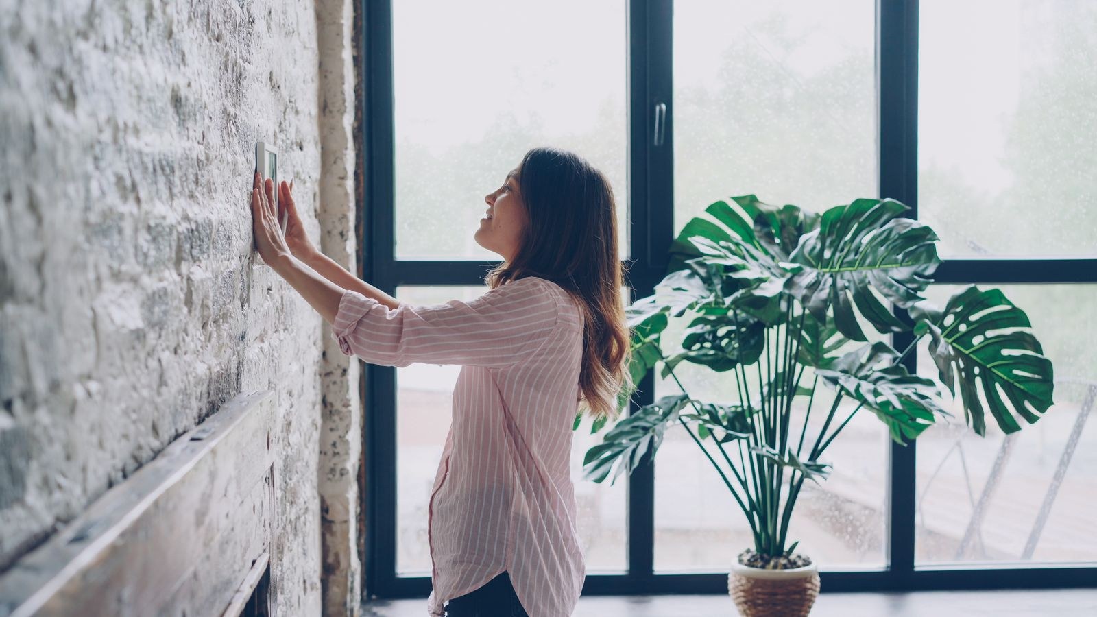 Woman adjusting a smart thermostat in a bright modern living room