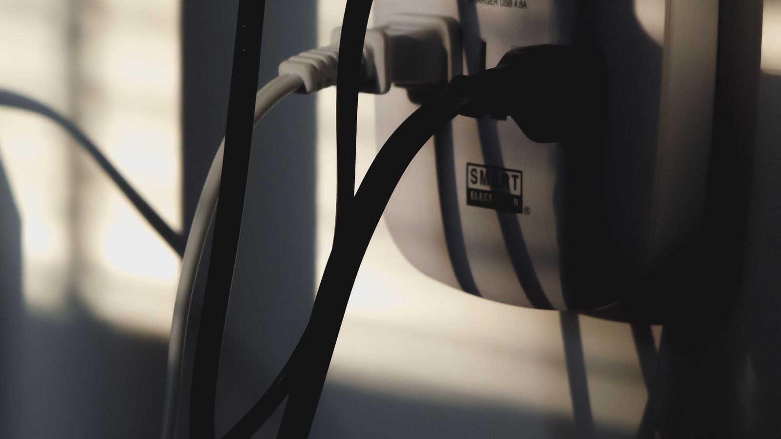 Multiple cables plugged into a wall outlet illustrating electrical load