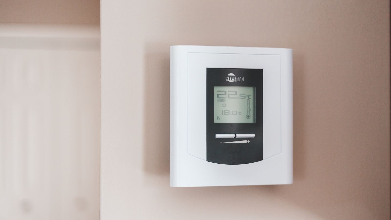 Person adjusting a wall-mounted home thermostat control
