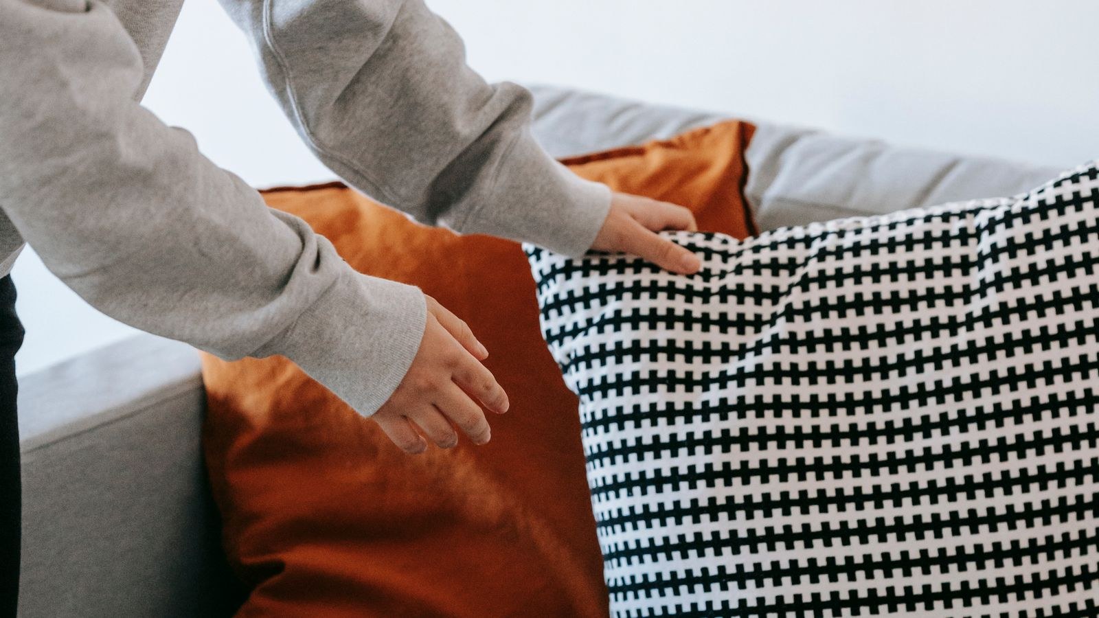Person fluffing and arranging cushions on a couch to maintain cushion loft