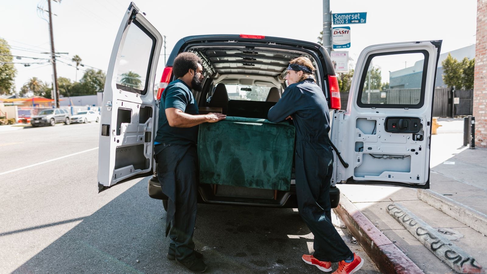 Movers loading a couch into a delivery van on a city street
