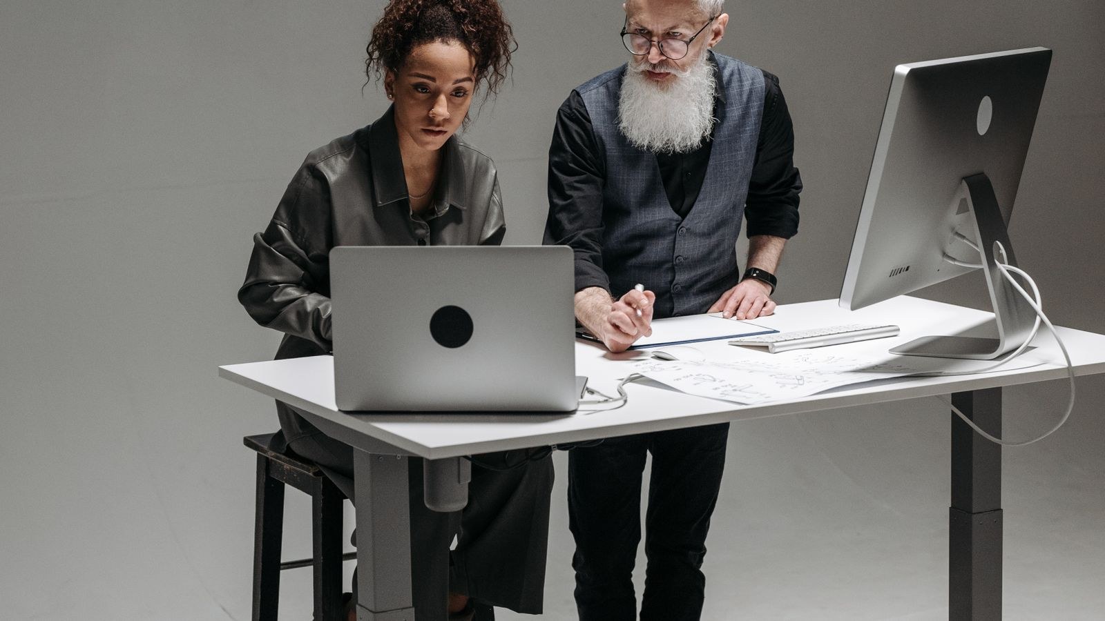 Two people working together at a standing desk with monitors and laptops