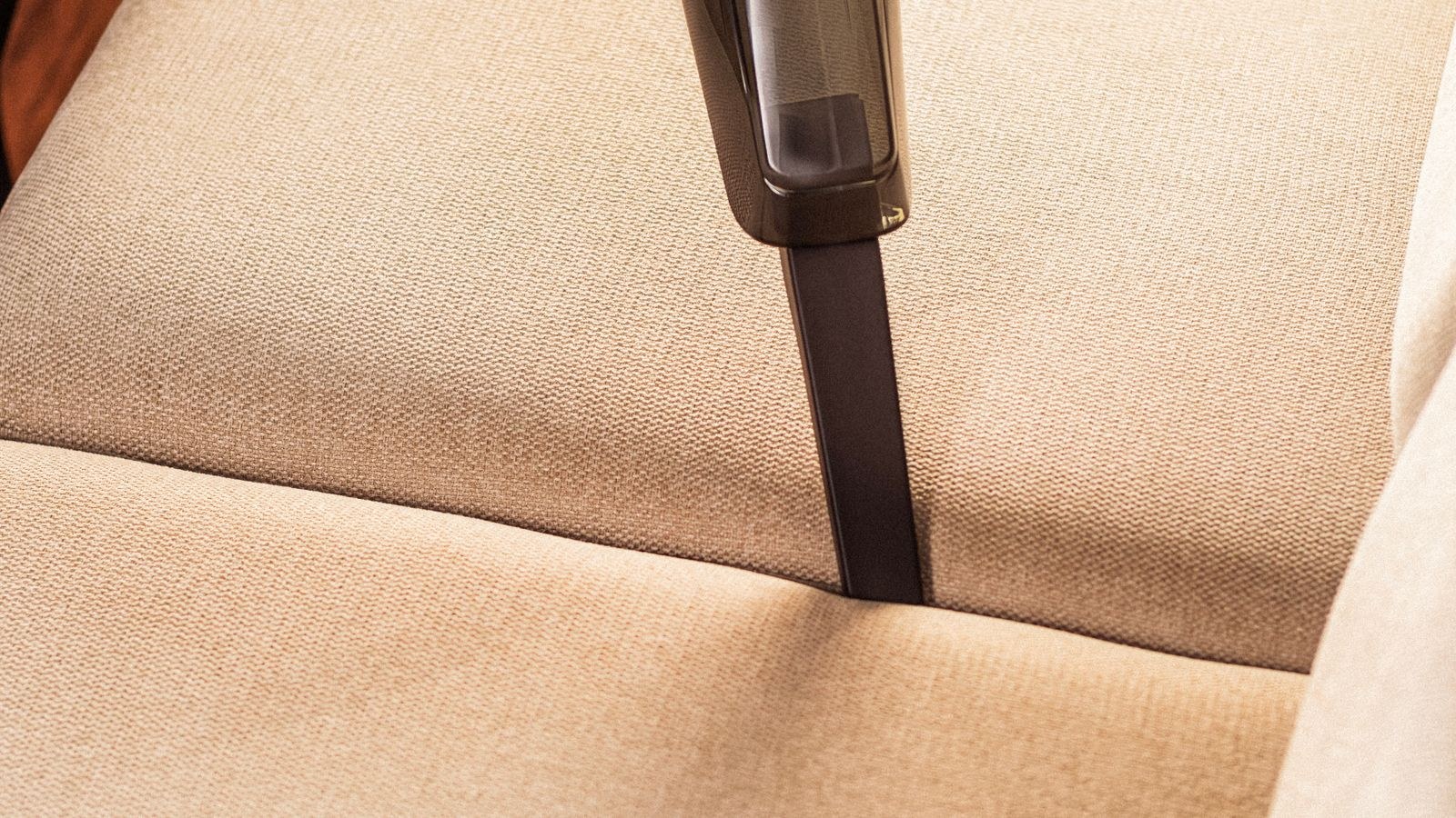 Handheld cordless vacuum cleaning a fabric sofa in a living room