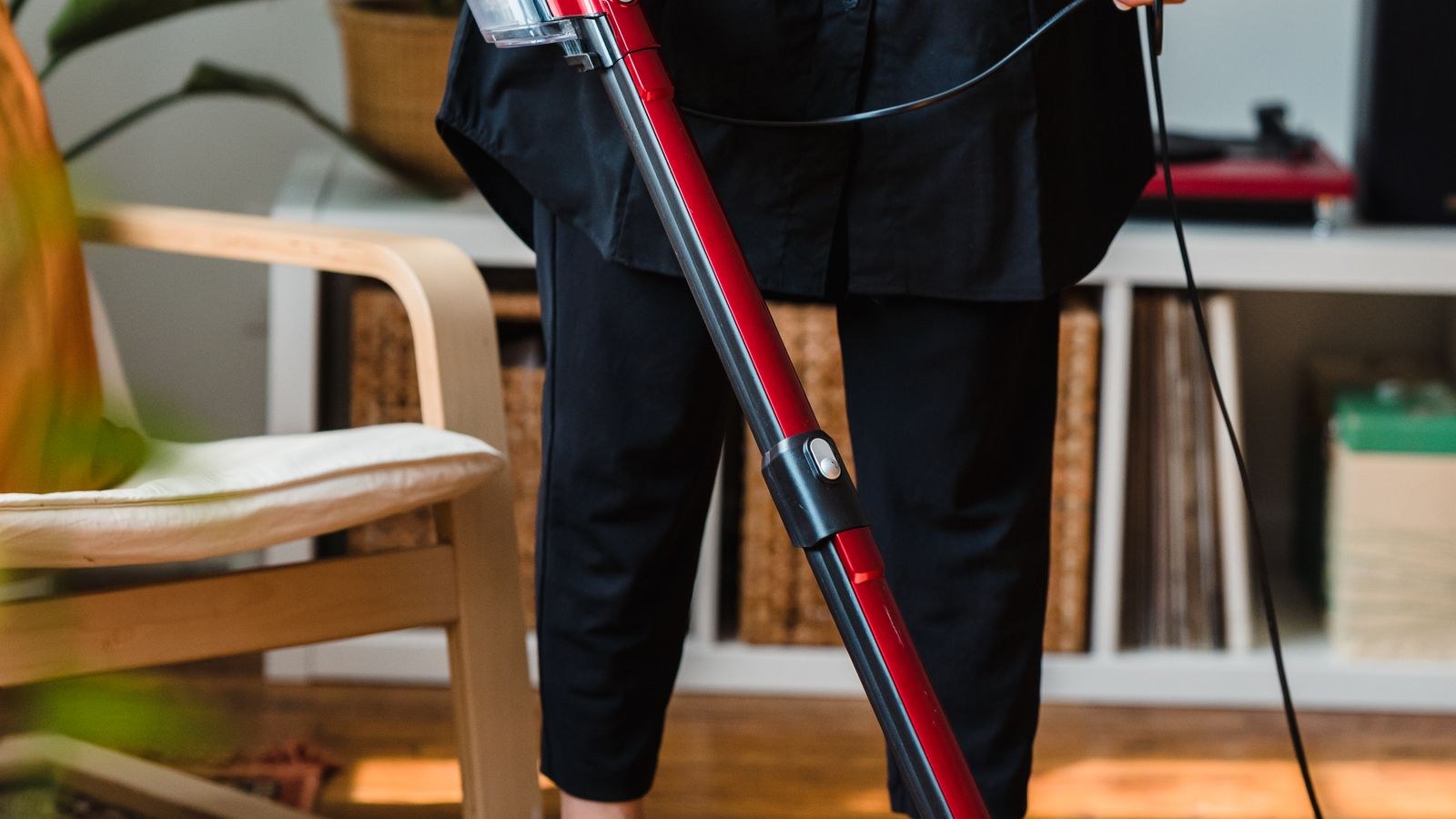 Cordless stick vacuum cleaning a wooden floor in a cosy living room