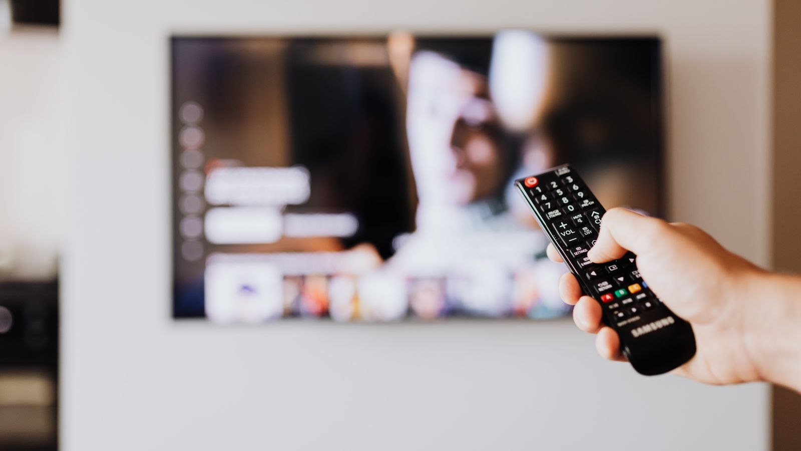 Person using a streaming stick remote with a smart TV home screen in the background