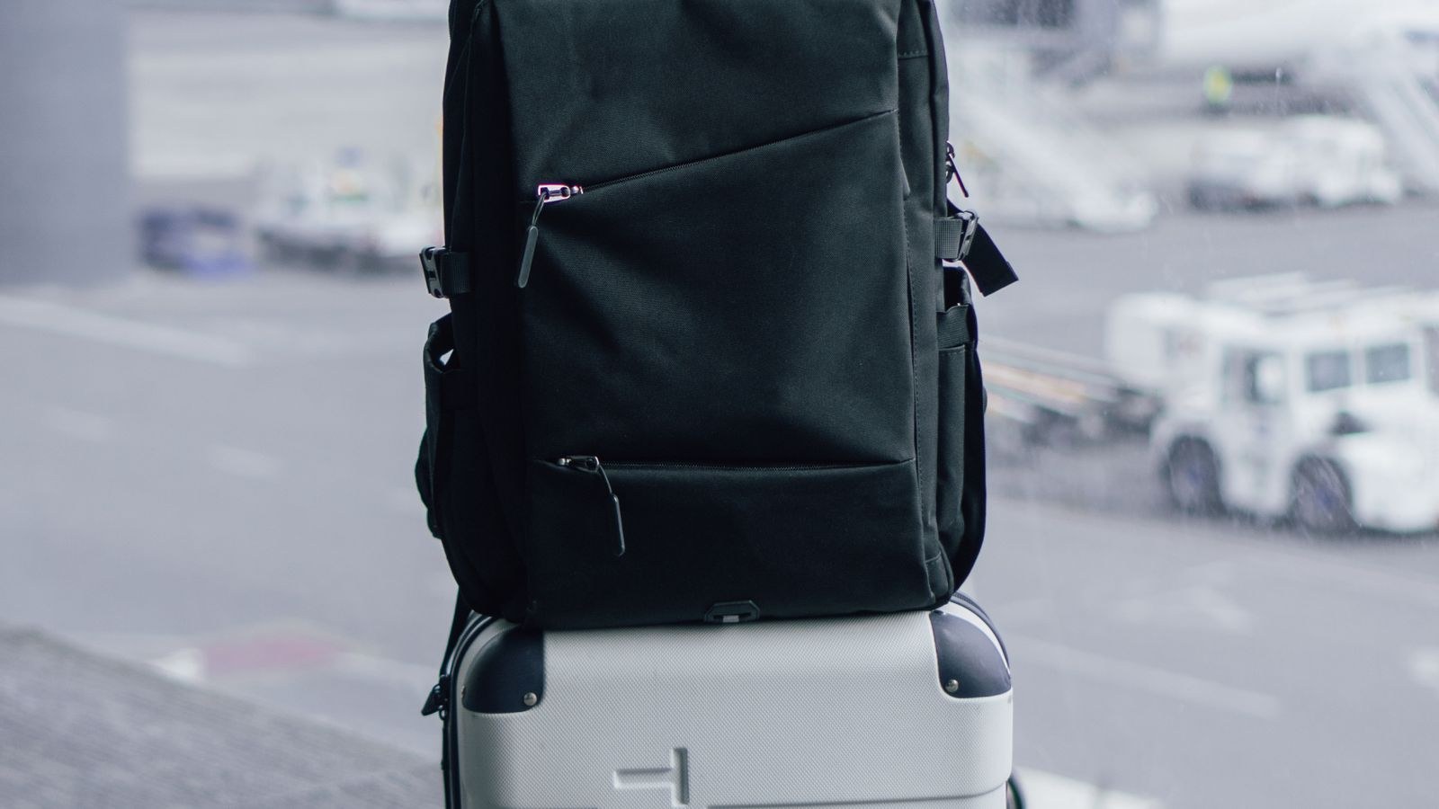 Black anti-theft travel backpack resting on a suitcase before a flight