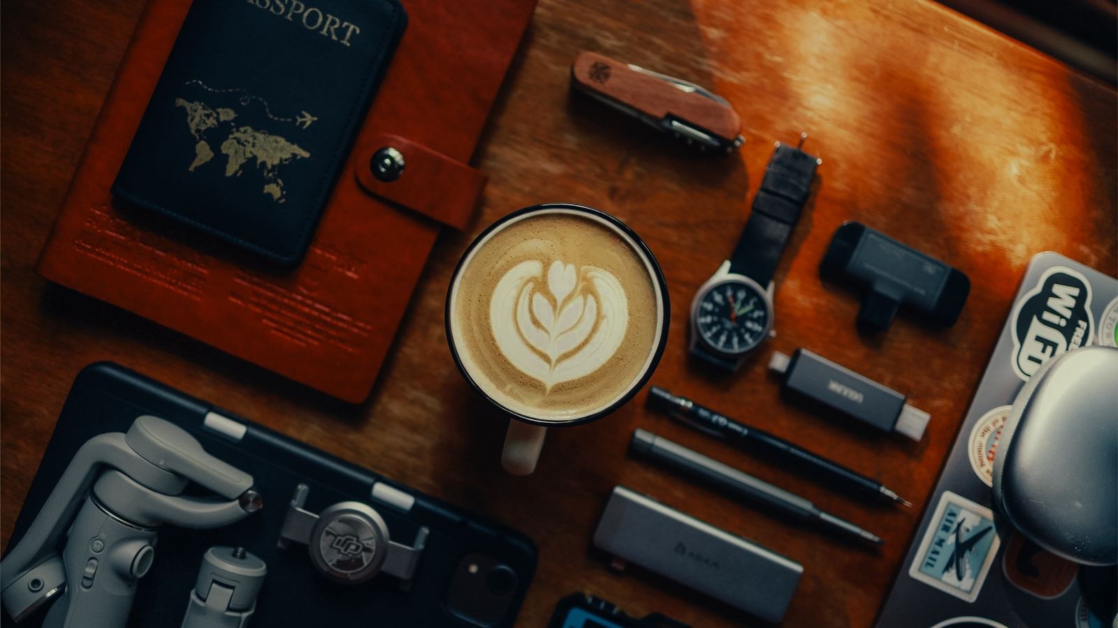 Flat lay of travel essentials including passport phone and tech accessories on a wooden table