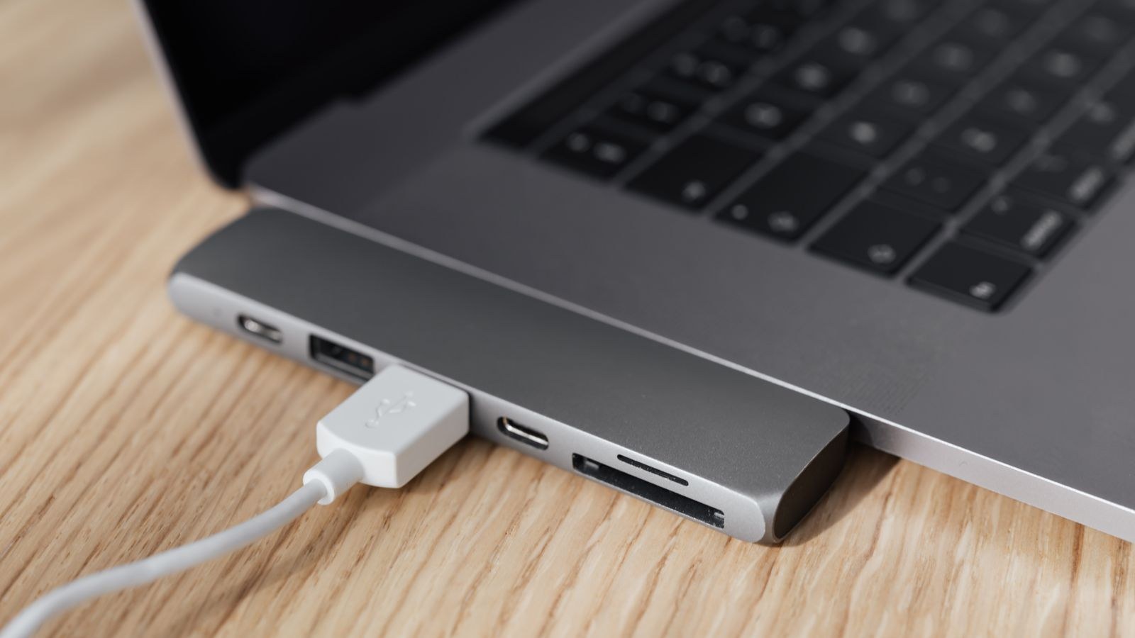 Laptop connected to a USB-C multiport hub with a white cable on a wooden desk