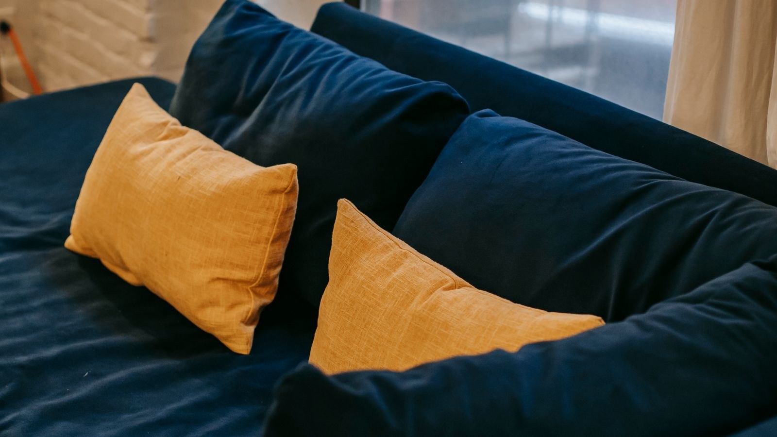 Blue fabric sofa with yellow cushions placed near a bright window