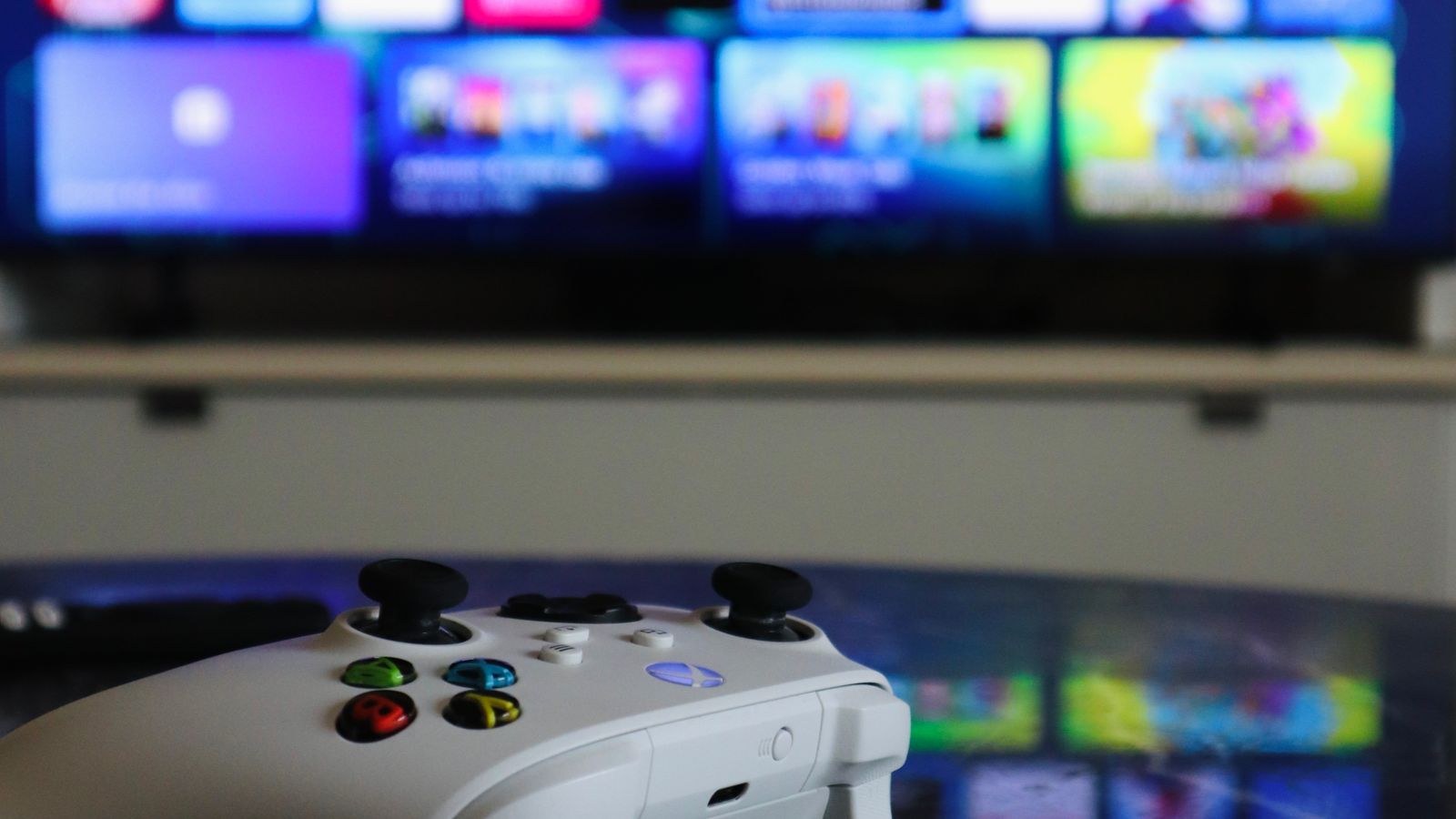 White gaming controller on a table with a TV displaying a game interface