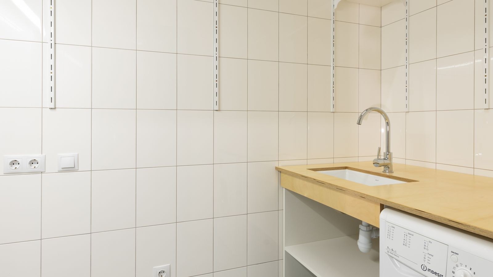Compact laundry area with washing machine, utility sink and open shelving in an apartment
