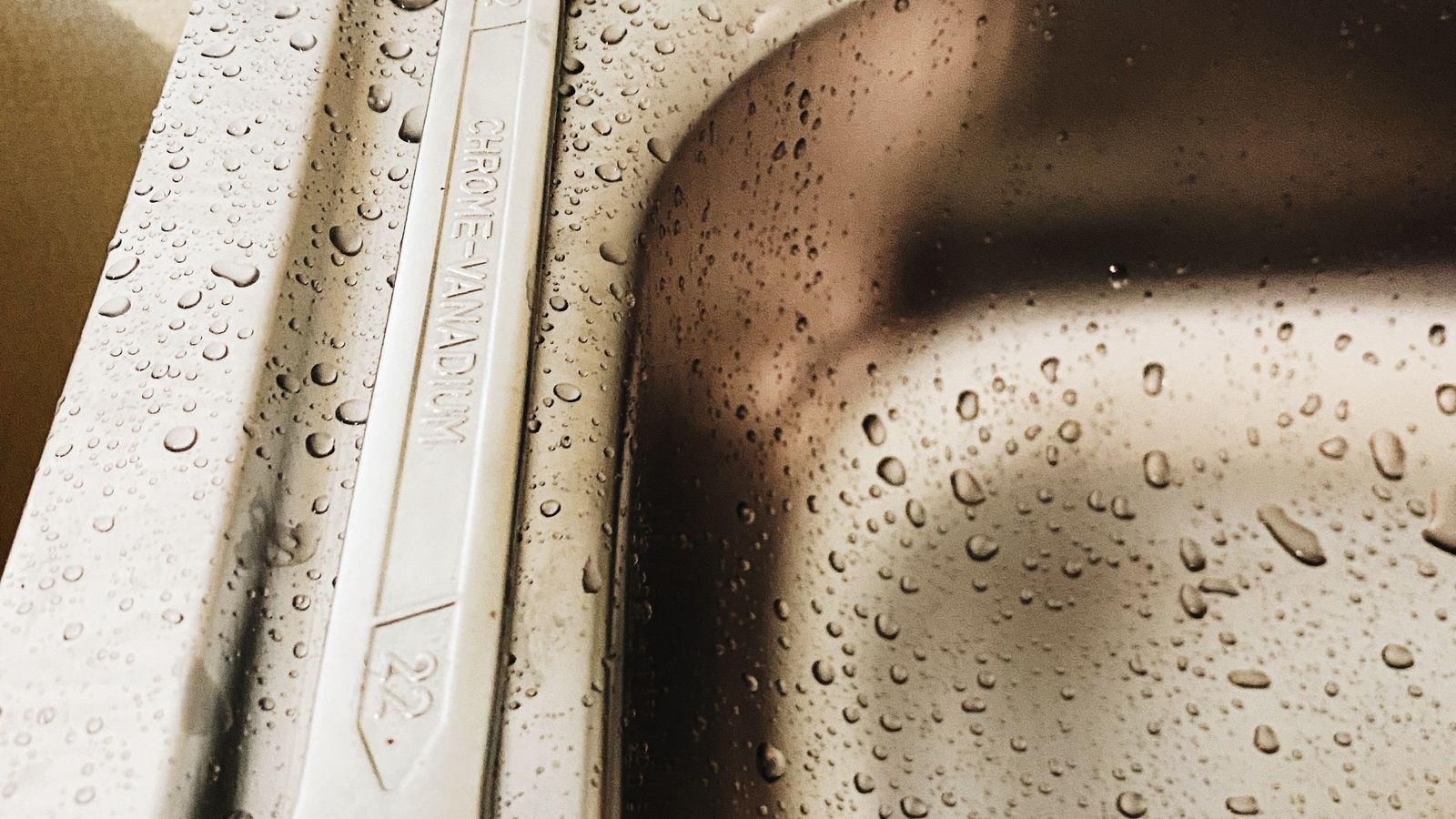 Plumbing wrench and water droplets on a sink, symbolizing leak repair and detection