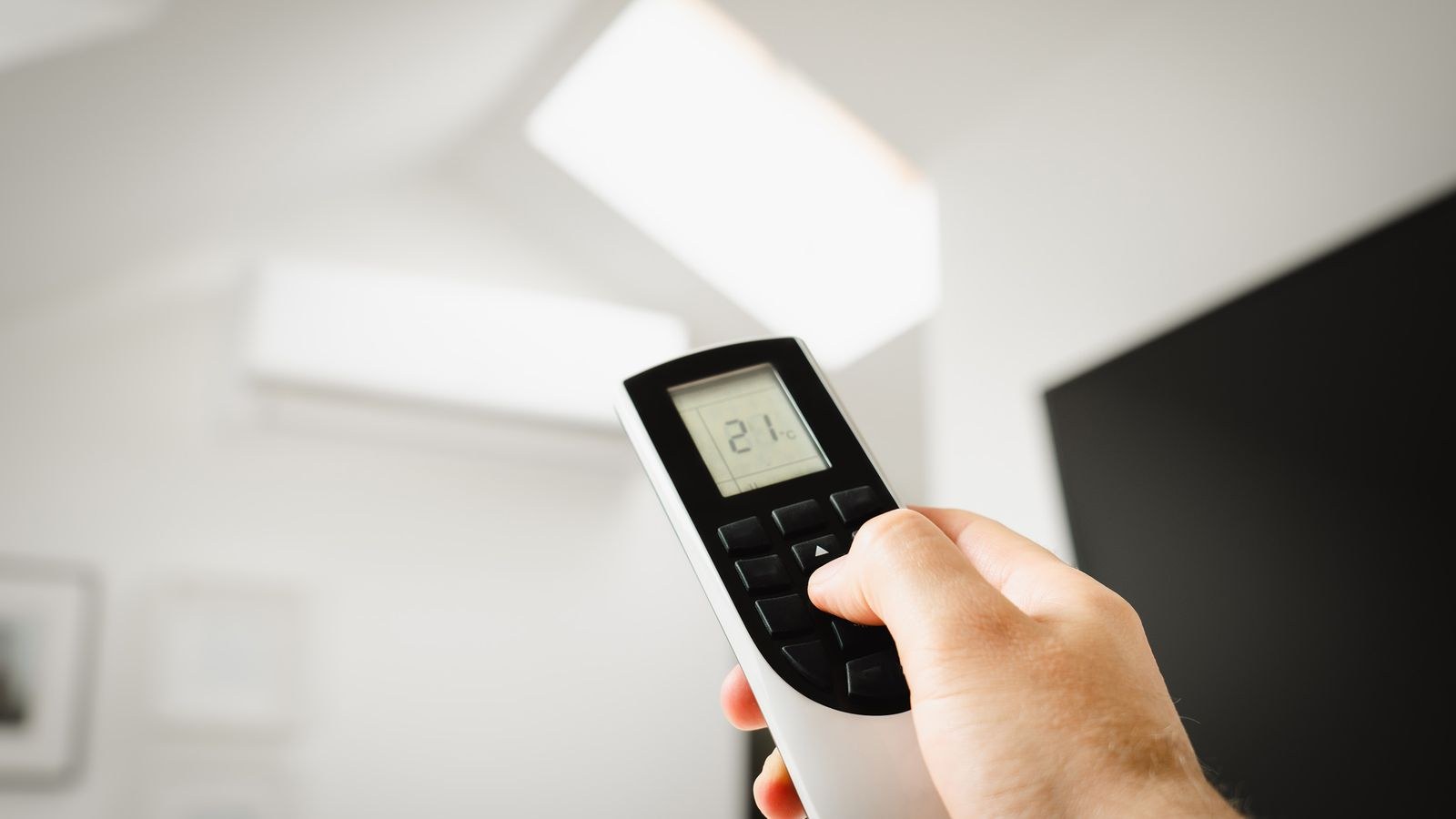 Hand using a remote control to adjust an indoor air conditioner