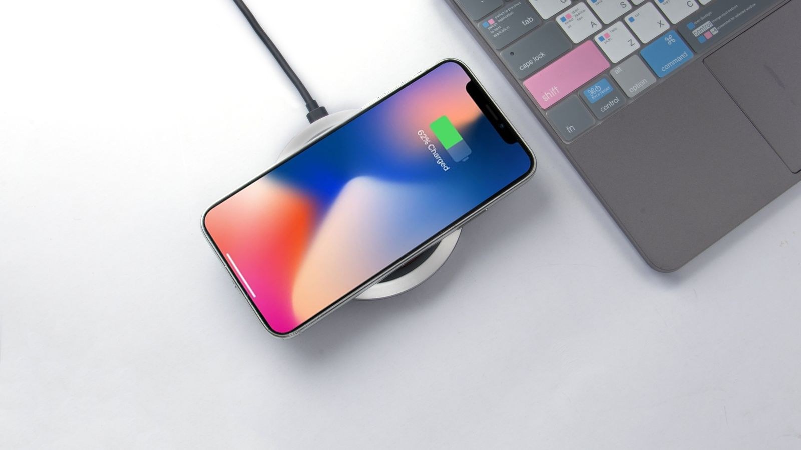 Smartphone charging wirelessly on a pad beside a laptop keyboard on a desk