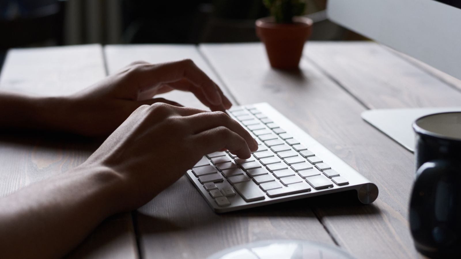 Hands typing on a wireless keyboard at a modern minimal workspace